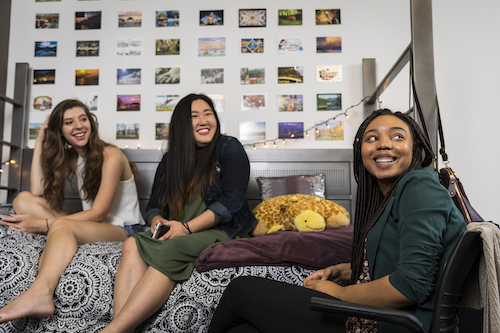 Students sitting on a bed in a residence hall room.