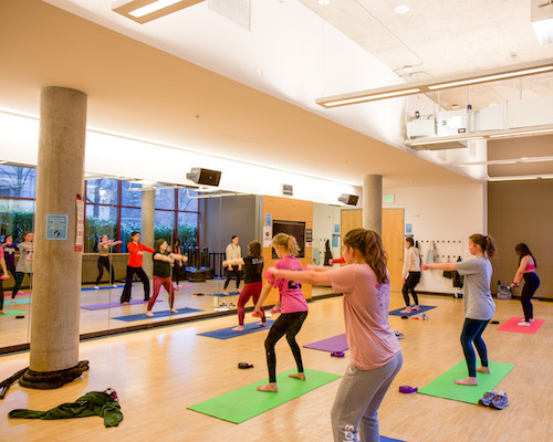 Students working out in a barre class in a studio on colorful mats.